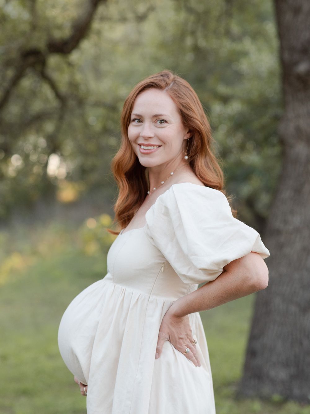Pregnant woman smiling during maternity photos in Central Texas with soft natural light and greenery