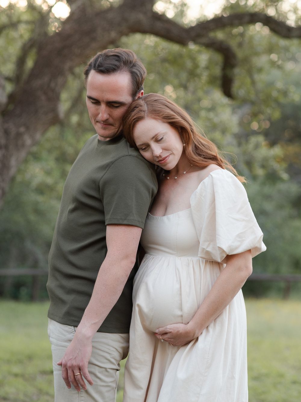 Expecting couple sharing quiet moment under trees during maternity photos in Central Texas with soft light