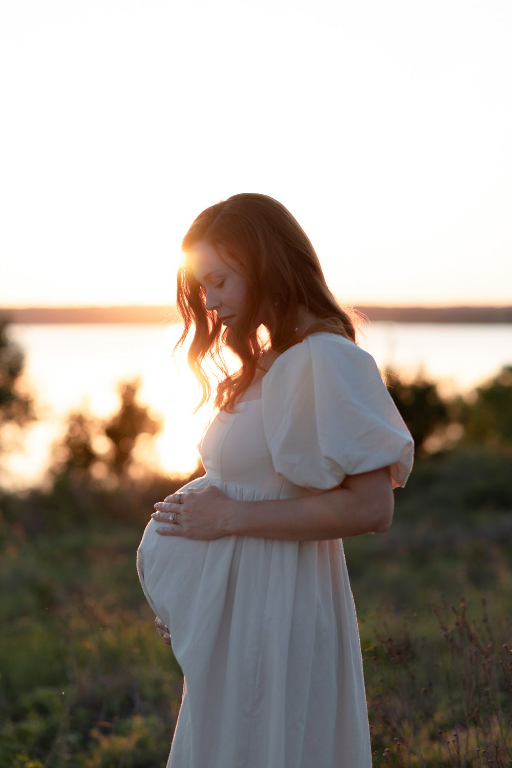 Expecting mother holding baby bump at sunset during outdoor maternity photos in Central Texas with warm golden light