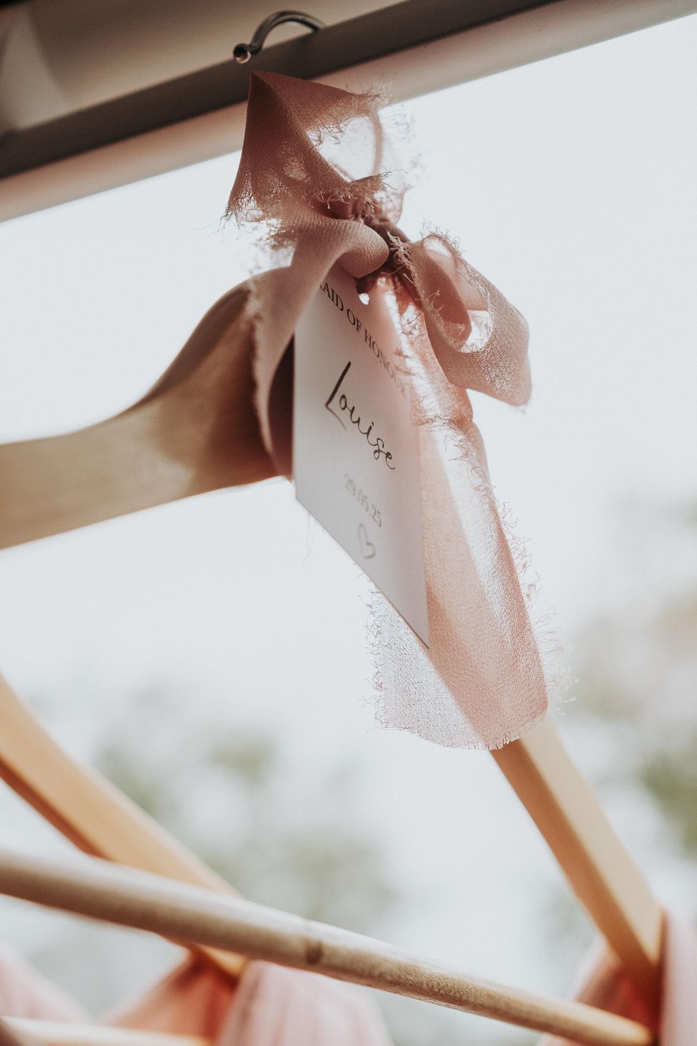 Wooden wedding hanger with pink satin ribbon bow and white bride tag, elegant bridal preparation detail.