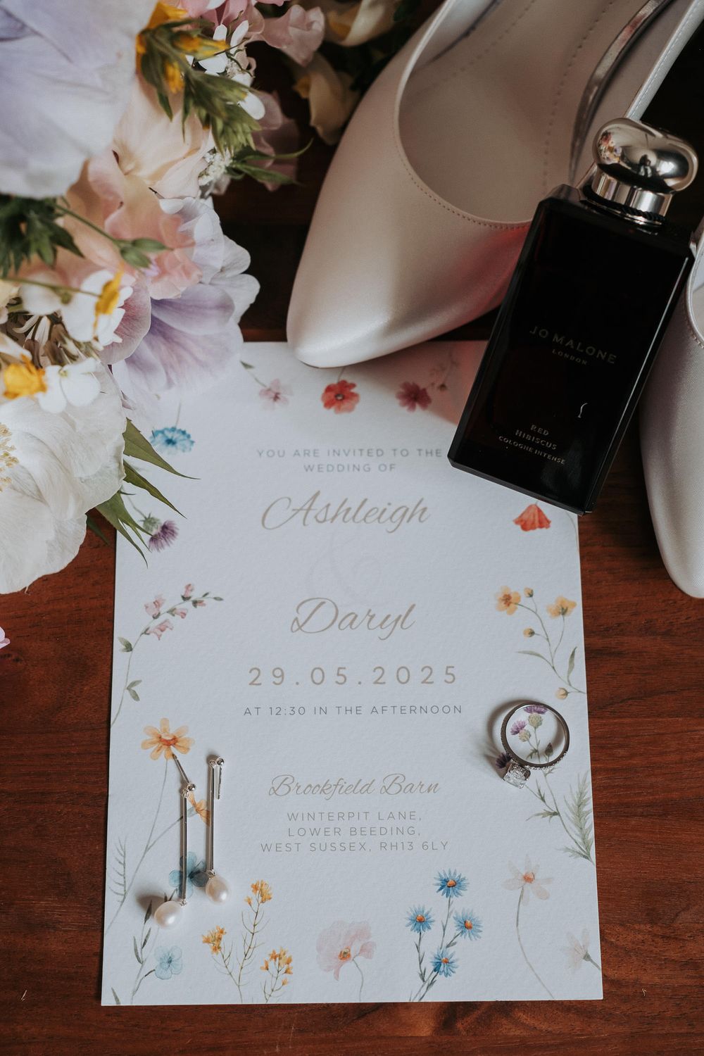 Wedding invitation for Ashleigh and Daryl on 29.05.2025 with floral design, rings, earrings and perfume.