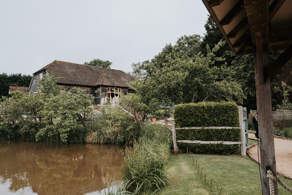 Charming countryside barn venue reflected in a tranquil pond surrounded by lush greenery.
