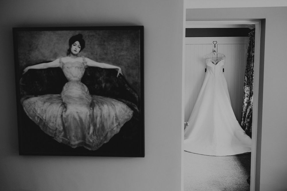 Black and white photo of a painting of a woman in a ballgown beside a doorway with a wedding dress hanging inside.