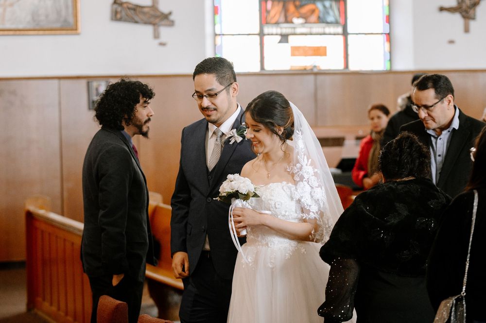 Bride in white lace gown and veil holds bouquet beside groom in suit during church wedding ceremony.