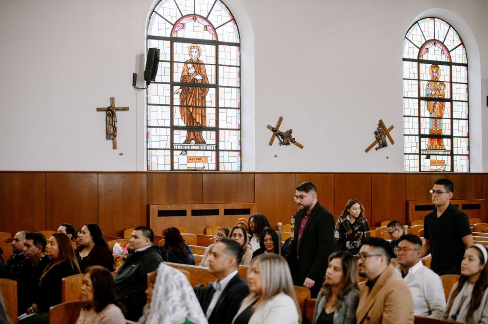 Congregation gathered in a modern Catholic church with stained glass windows during a religious service.
