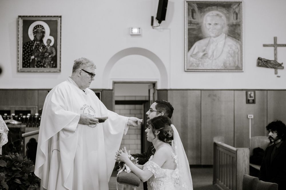 Priest officiating a wedding ceremony in a church with religious portraits on the wall behind him.