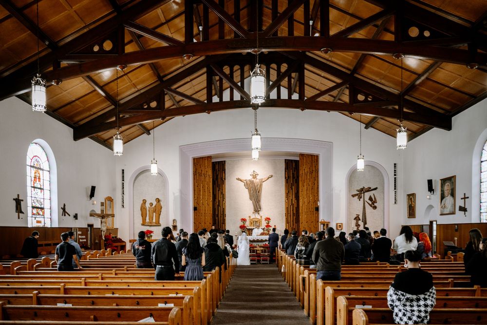 Wedding ceremony in a rustic Catholic church with wooden pews, vaulted ceiling, and a crucifix altar.