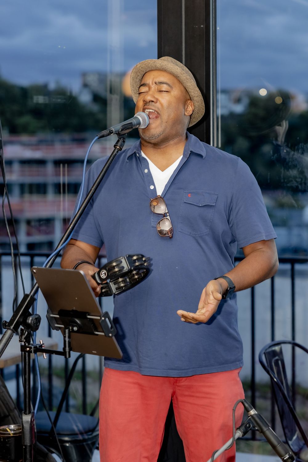 Man in blue polo and red pants singing passionately at microphone stand outdoors at dusk.