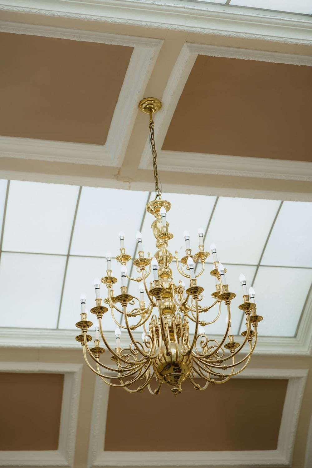 Elegant gold chandelier with multiple candle-style lights hanging from a coffered ceiling in a grand interior.