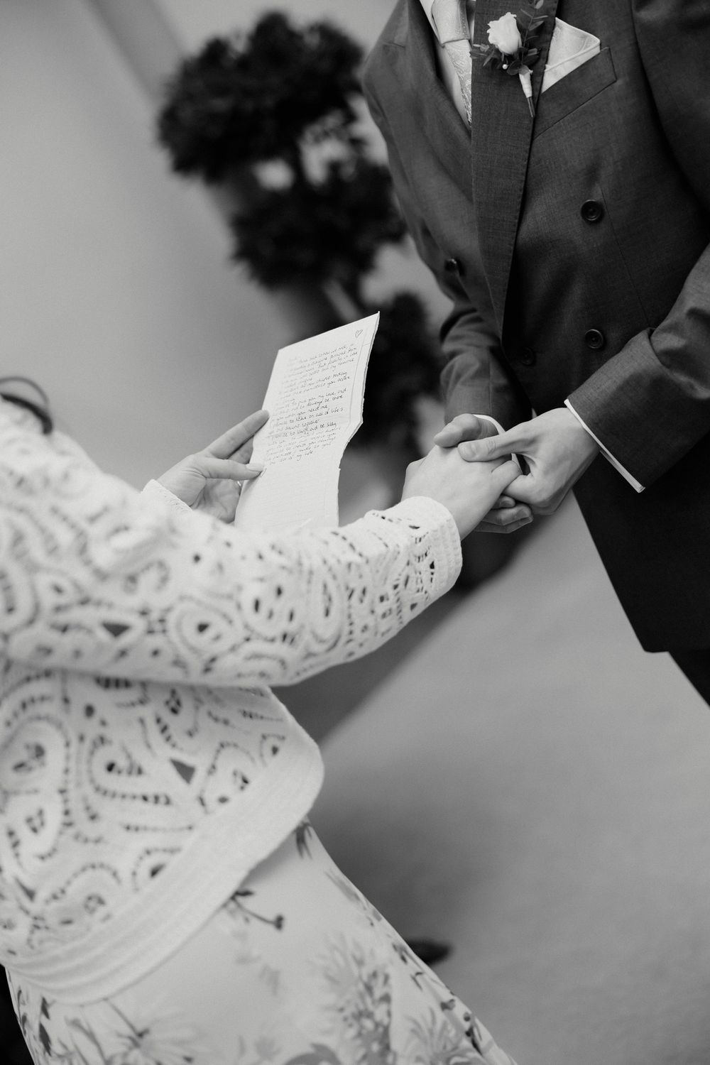 Black and white photo of bride and groom exchanging vows and holding hands during wedding ceremony.