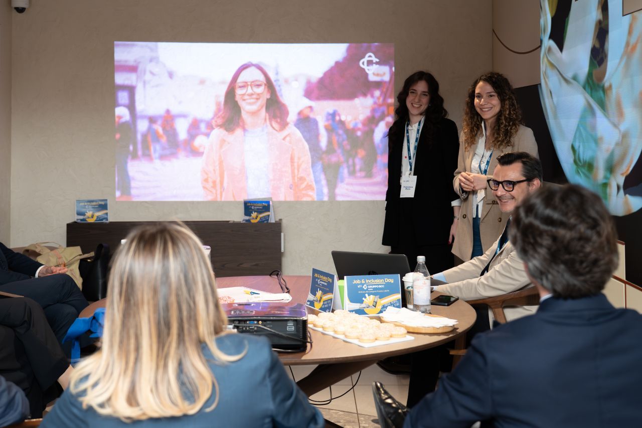 Business professionals attend a presentation with a projected screen showing a smiling woman in an orange jacket.