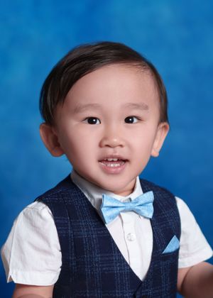 Young boy in navy plaid vest and light blue bow tie smiling for a school portrait photo.