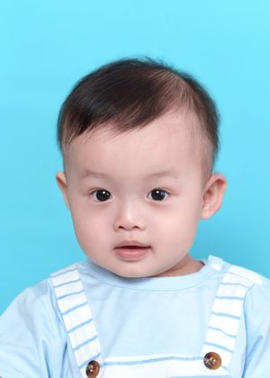 Cute Asian baby boy with dark hair wearing a light blue striped outfit, photographed against a bright turquoise background.