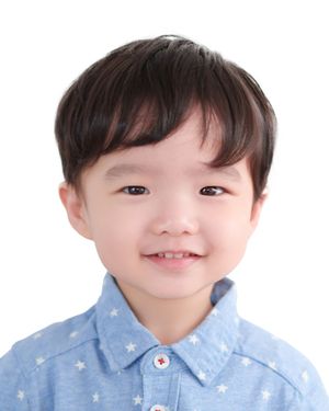 Smiling young Asian boy with dark hair wearing a light blue star-patterned shirt, portrait photo on white background.