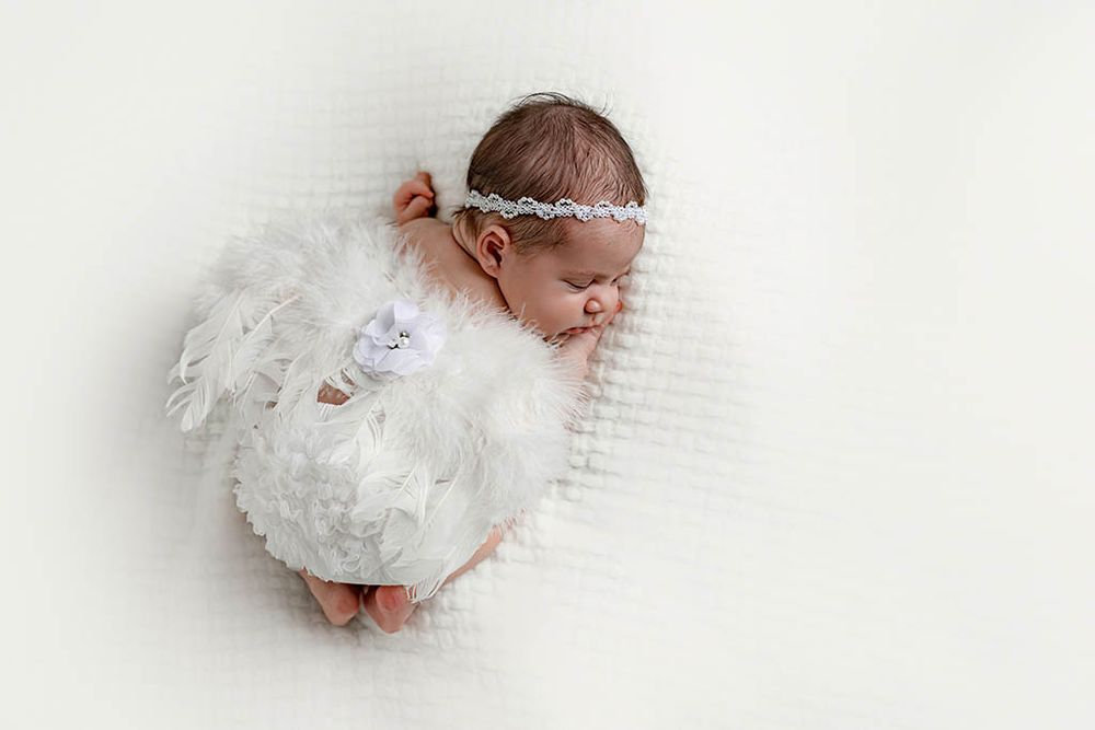 Affordable newborn photographer near Winchester CA: Newborn baby girl sleeping in white feather angel wings and floral headband.