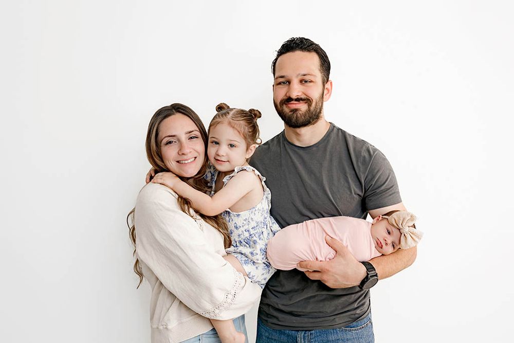 Winchester CA Family and newborn photographer photo of family of four posing together, parents holding toddler and newborn baby girls.