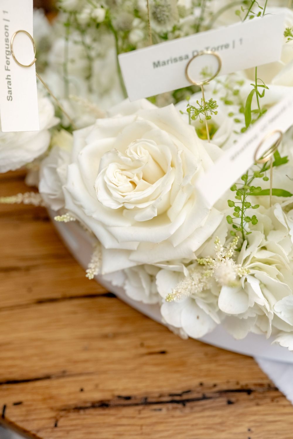 White roses and hydrangeas wedding table centerpiece with place cards on rustic wood table.