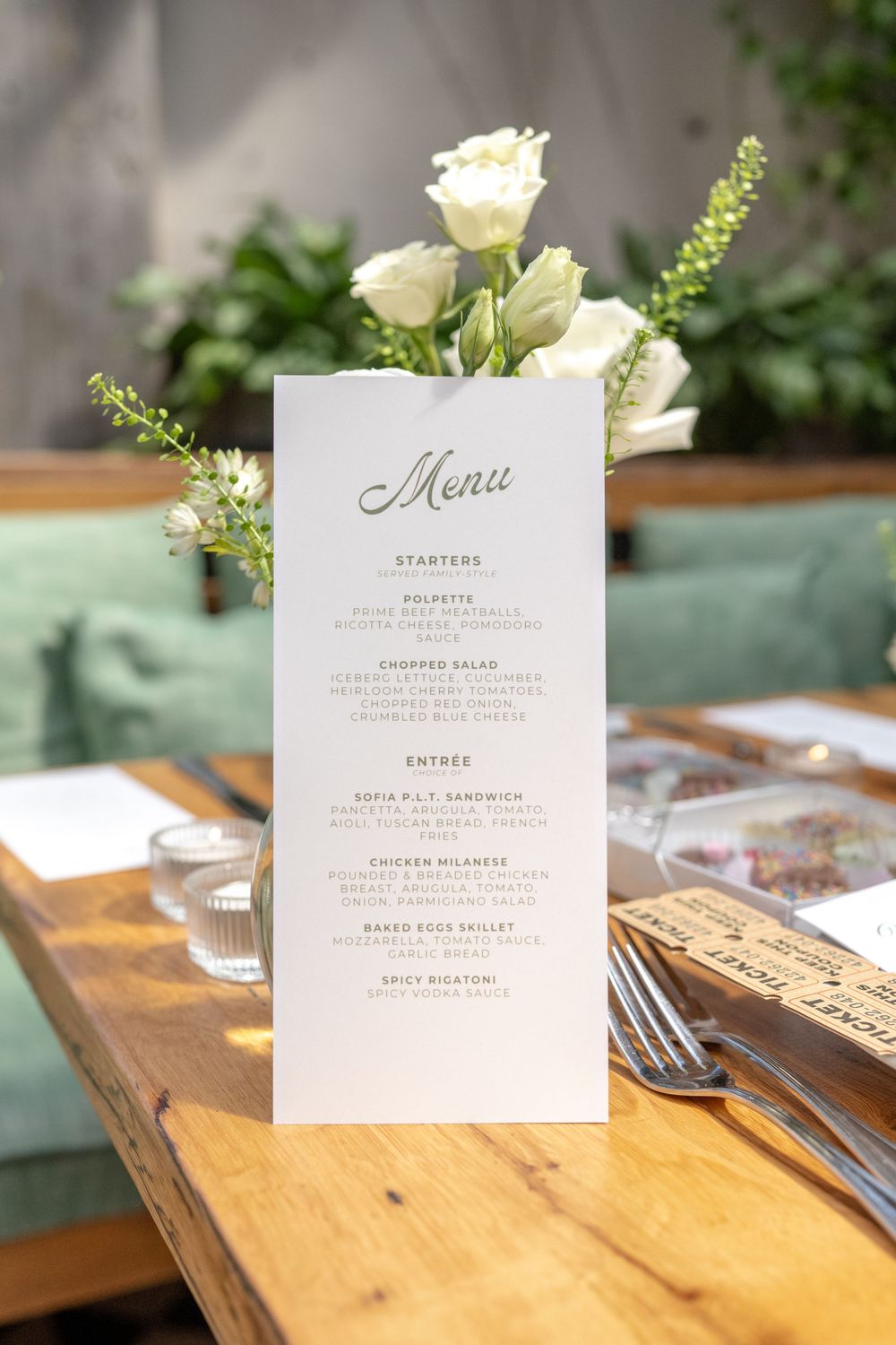 Elegant wedding menu card displayed on wooden table with white roses and greenery at a restaurant reception.