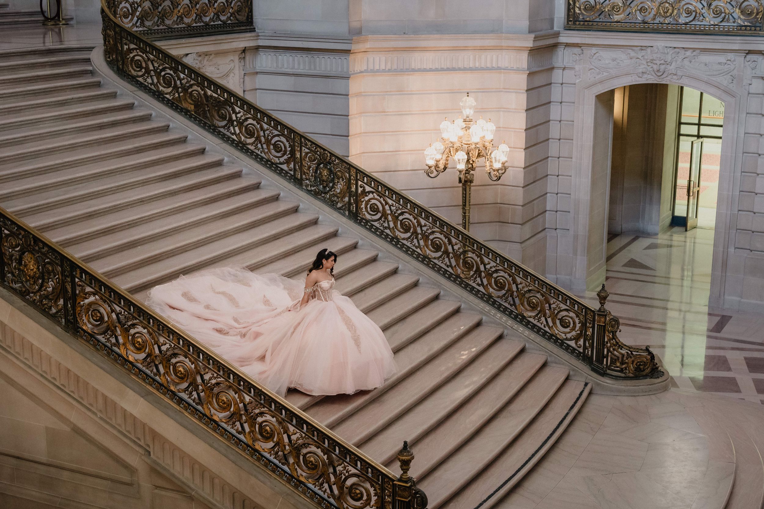Bride in ballgown poses on lush lawn before a stunning white castle venue with Gothic arched windows and gold doors.