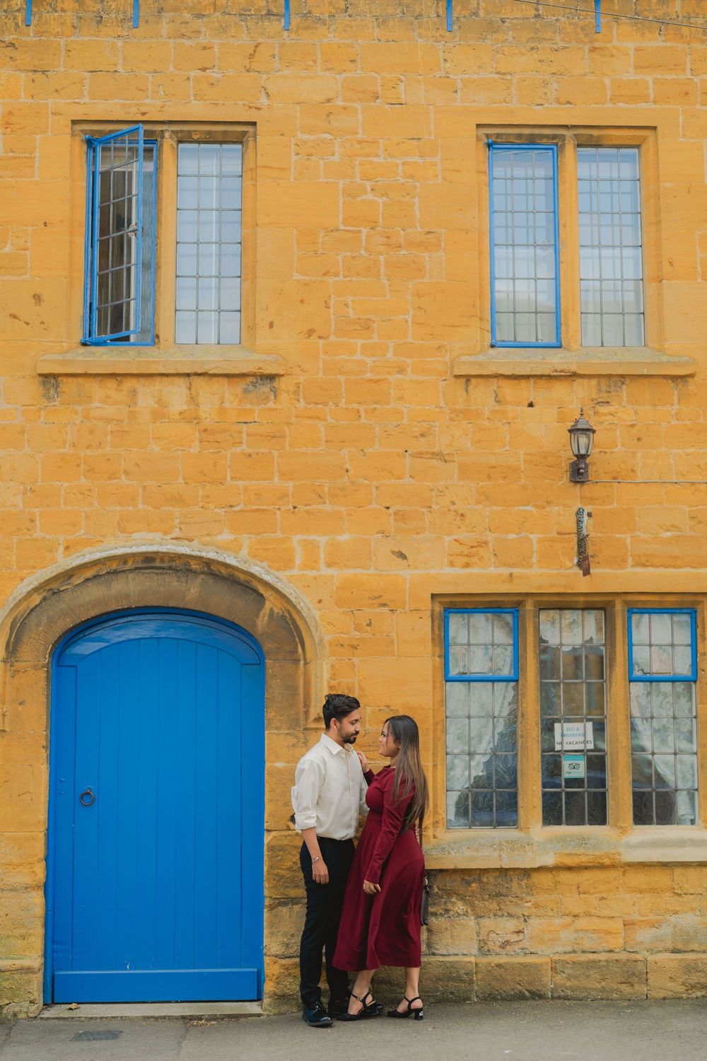 Couple standing together by a blue arched door on a golden stone building with blue-framed windows.