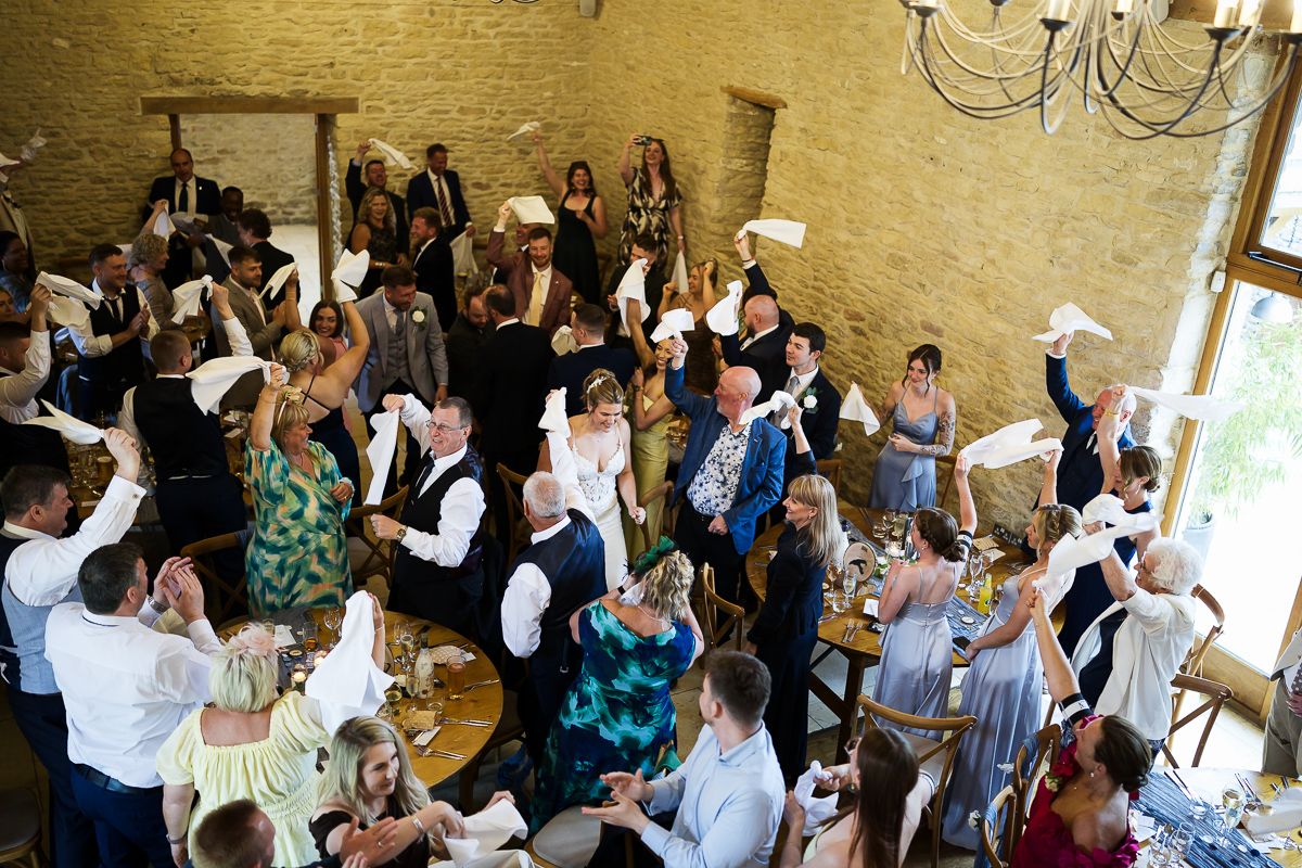 Overhead view of a wedding reception with guests mingling in an elegant venue with chandelier and stone walls.