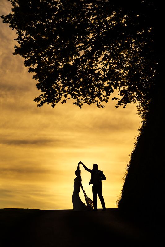 Silhouette of bride and groom dancing under a tree at golden sunset on their wedding day.