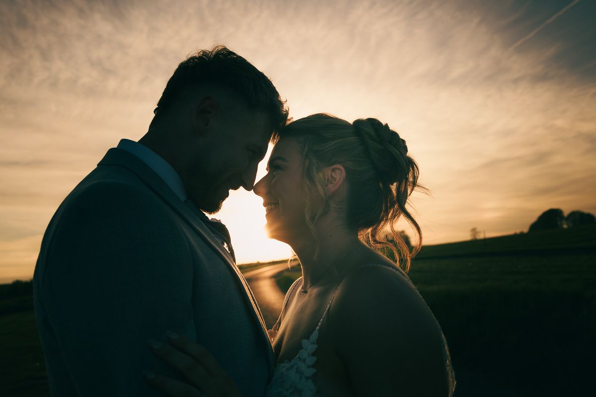A couple shares a romantic sunset moment, silhouetted against a golden sky on their wedding day.