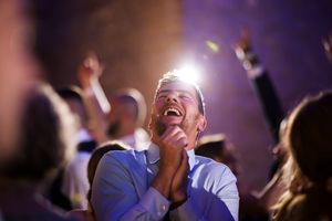 Excited man clapping and laughing at a concert, bathed in bright stage light among a cheering crowd.