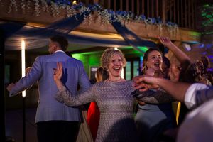 Guests dancing joyfully at a wedding reception, with colorful lights and floral decorations in the background.