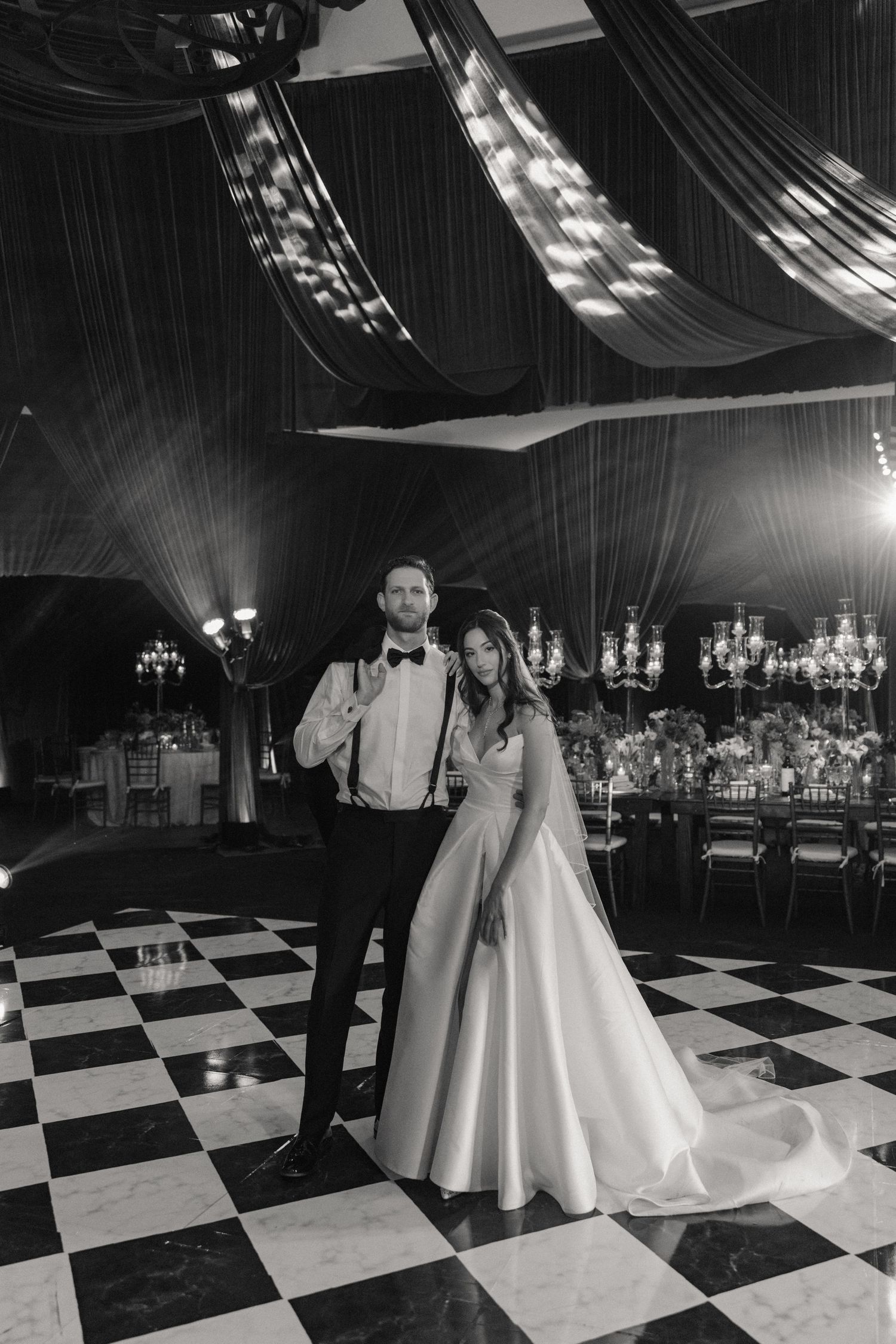 Bride and groom pose on checkered dance floor in elegant black and white wedding reception photo.