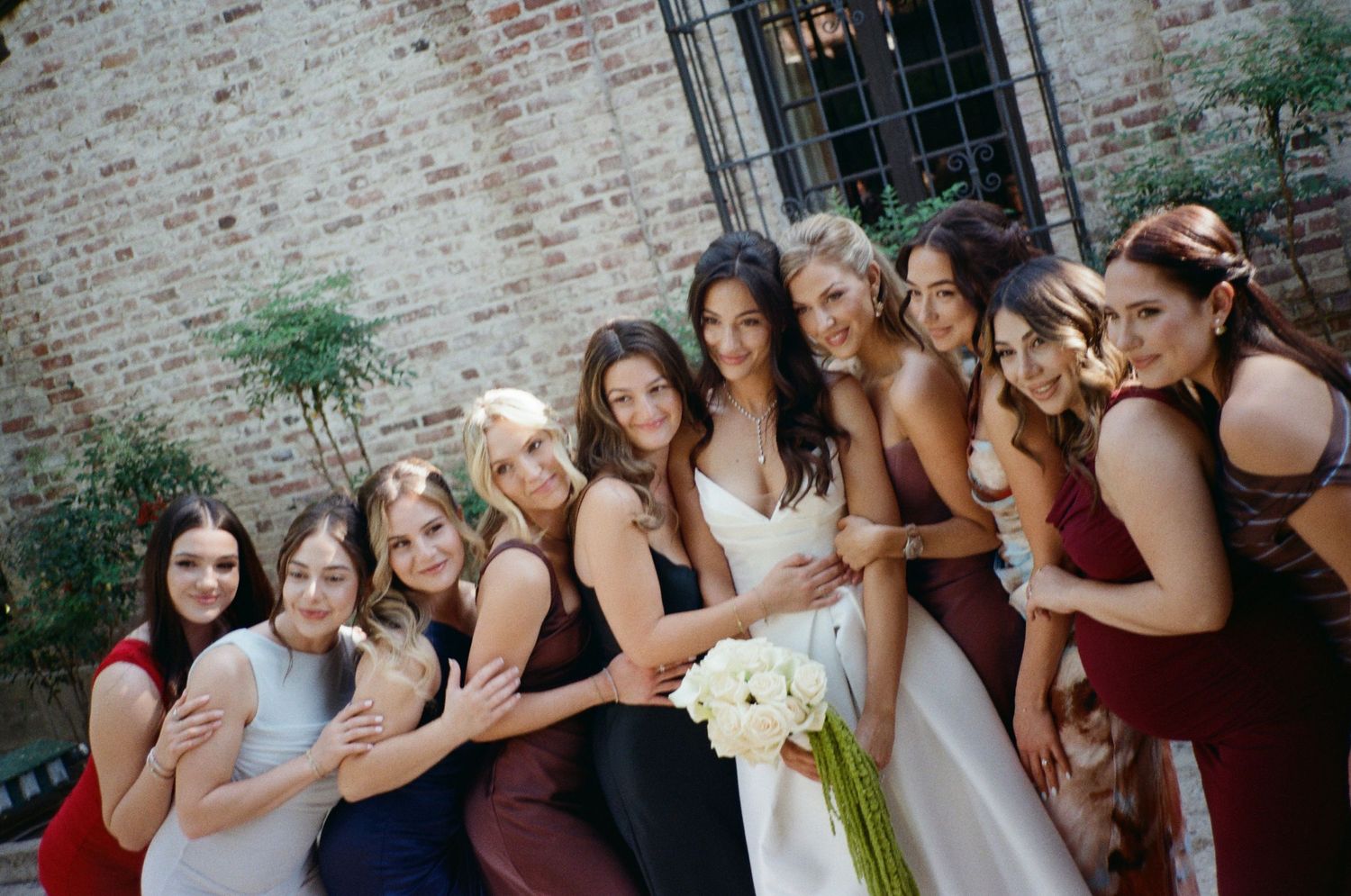 Bride in white gown poses with bridesmaids in burgundy and navy dresses holding white bouquet.