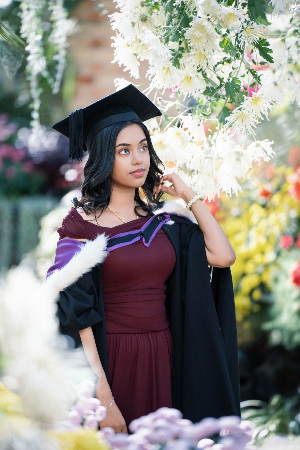 A proud graduate posing next to vibrant greenhouse flowers in the Winter Garden, Auckland Domain for her graduation photos.