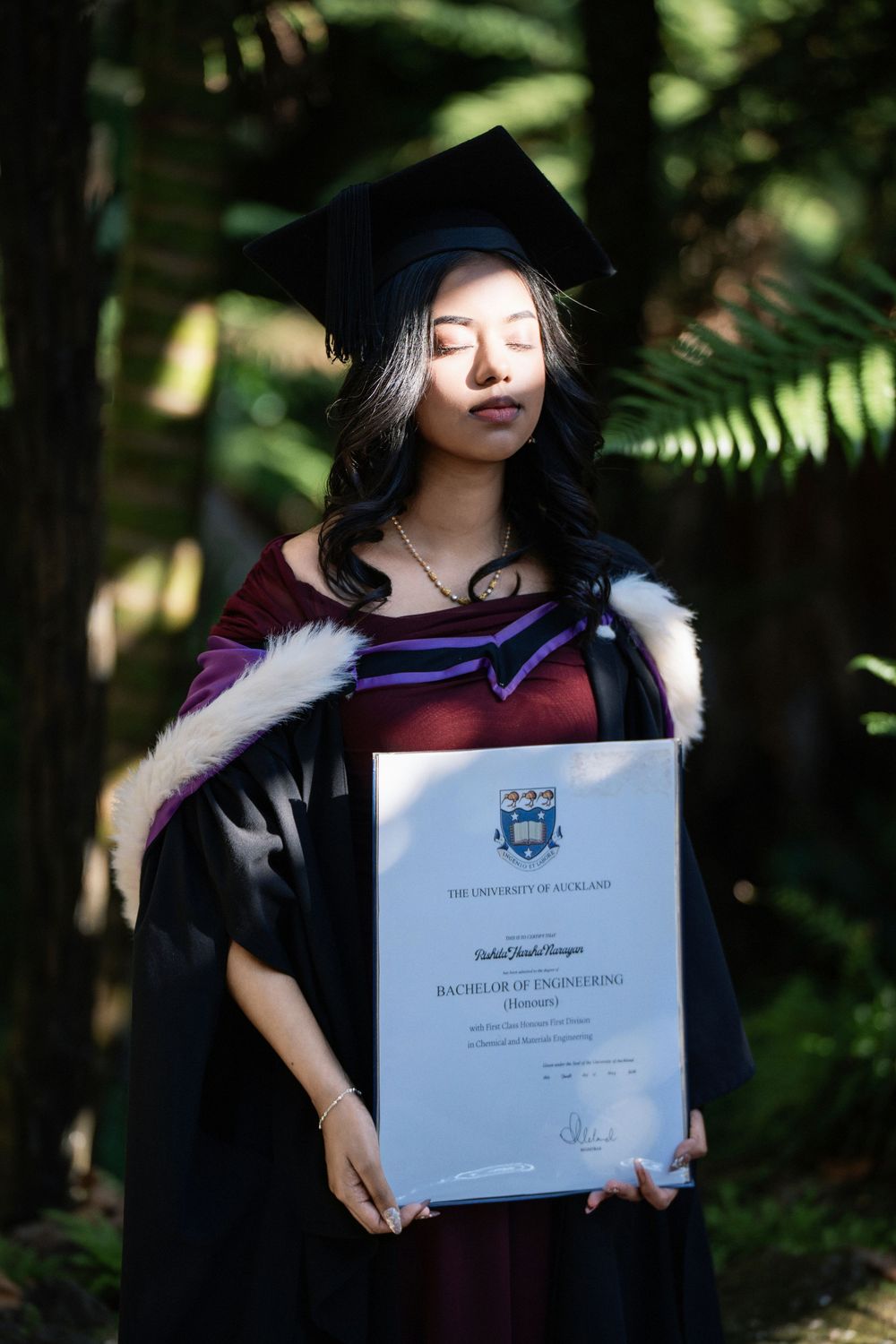 Cinematic portrait of a graduate holding her diploma under a shaded tree in Auckland Domain.