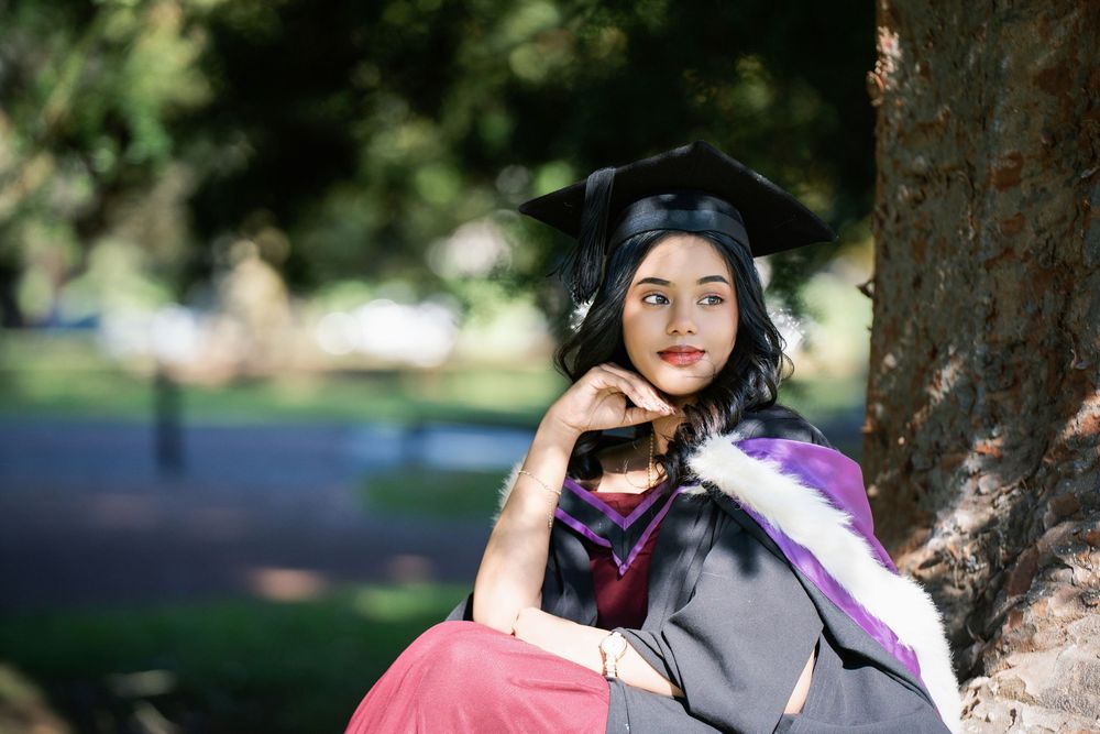 A graduate resting gracefully against a tree trunk in the scenic Auckland Domain for her graduation photography.