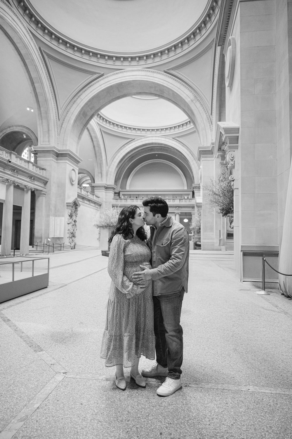 Black and white photo of a couple kissing inside the Metropolitan Museum of Art under grand arched ceilings.