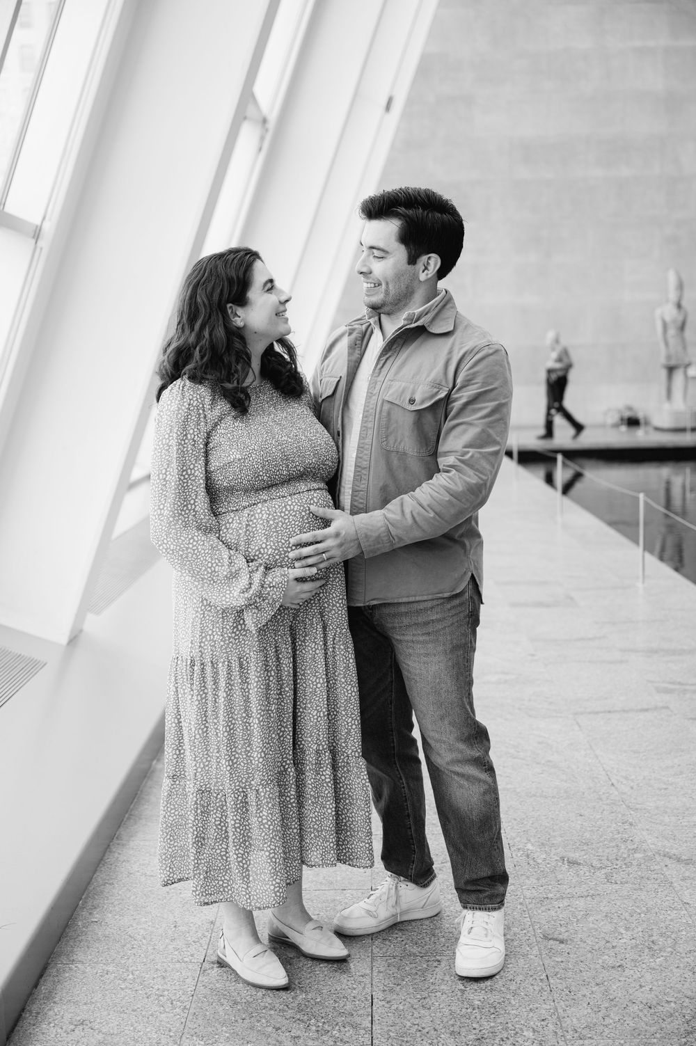 Black and white photo of a smiling couple sharing a tender moment, with the man gently holding the womans pregnant belly.