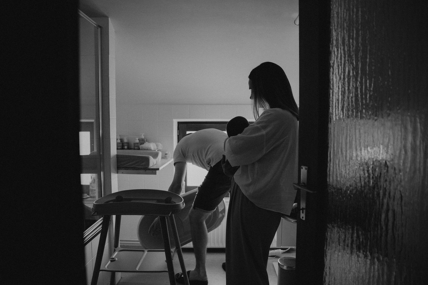 Black and white photo of a mother holding her baby by a window.