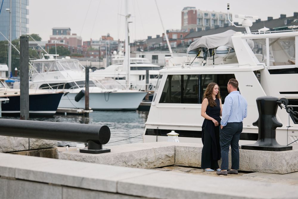 Couple standing on a waterfront dock surrounded by luxury yachts at a marina, ideal for engagement photos.
