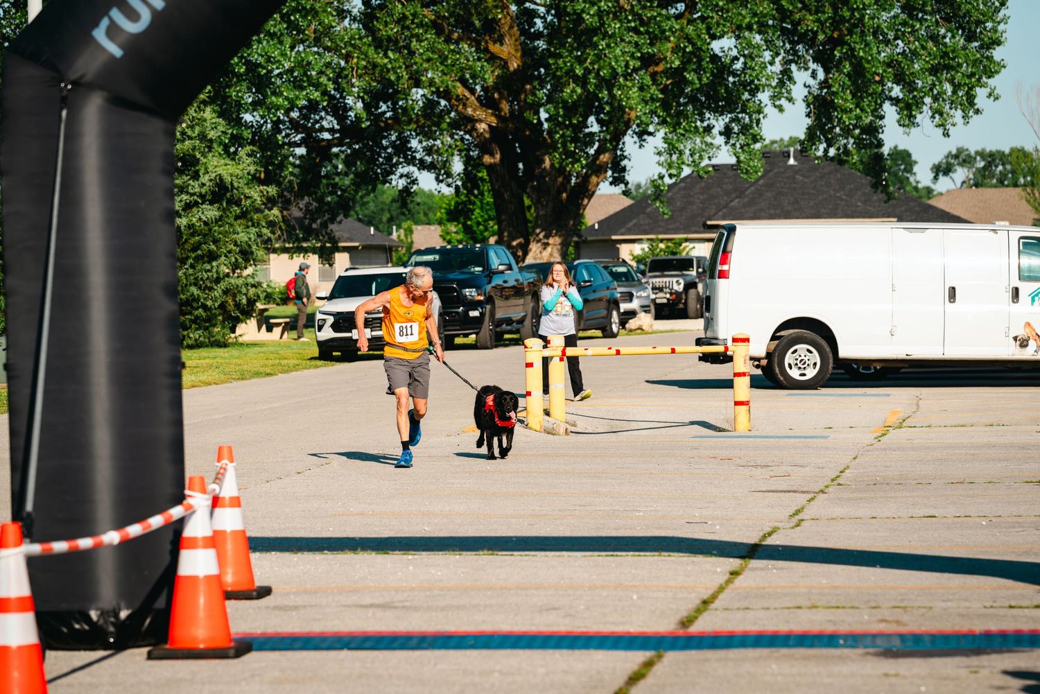 Runner with a black dog on a leash crossing the finish line at an outdoor 5K race event.