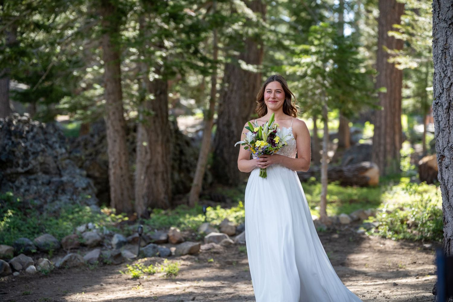 Couple sharing umbrella in rain, bride holding sunflowers in white gown, groom in gray suit.