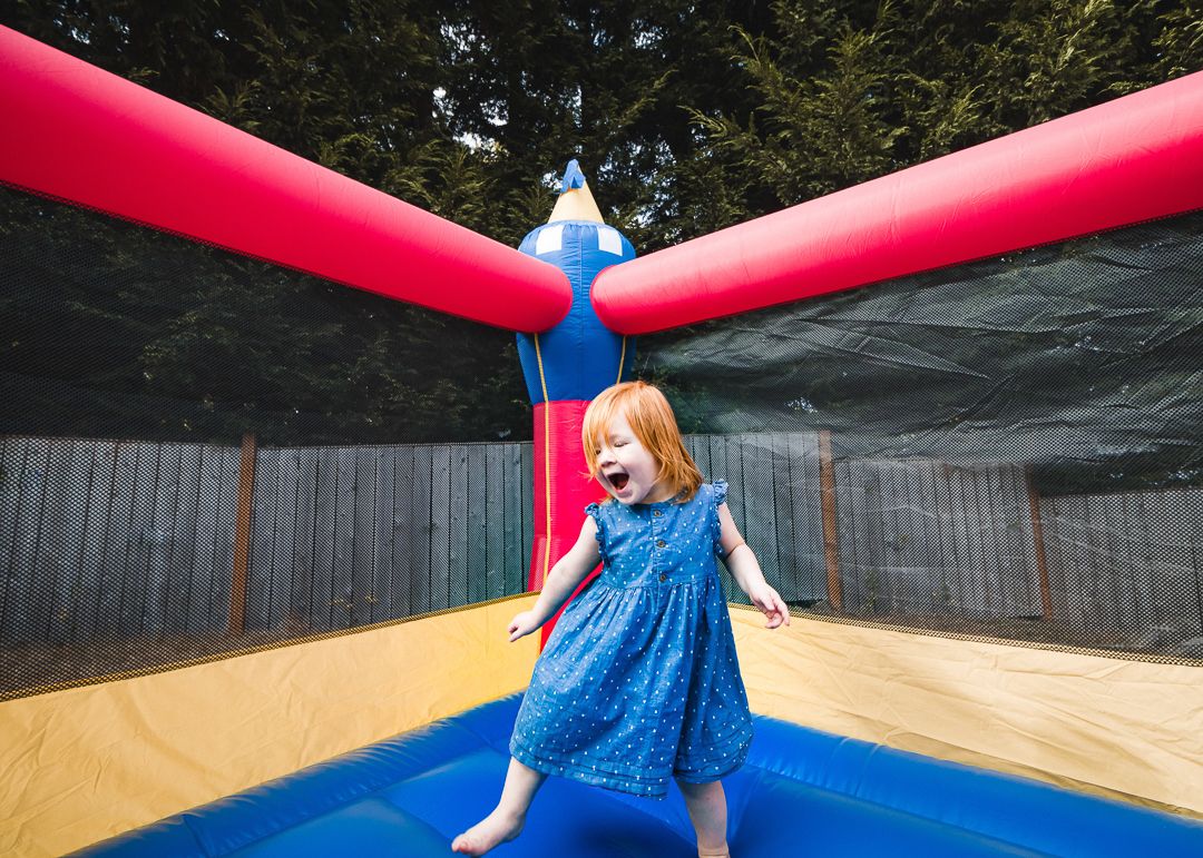 Young red-haired girl laughing joyfully while bouncing in a colorful inflatable bounce house outdoors.