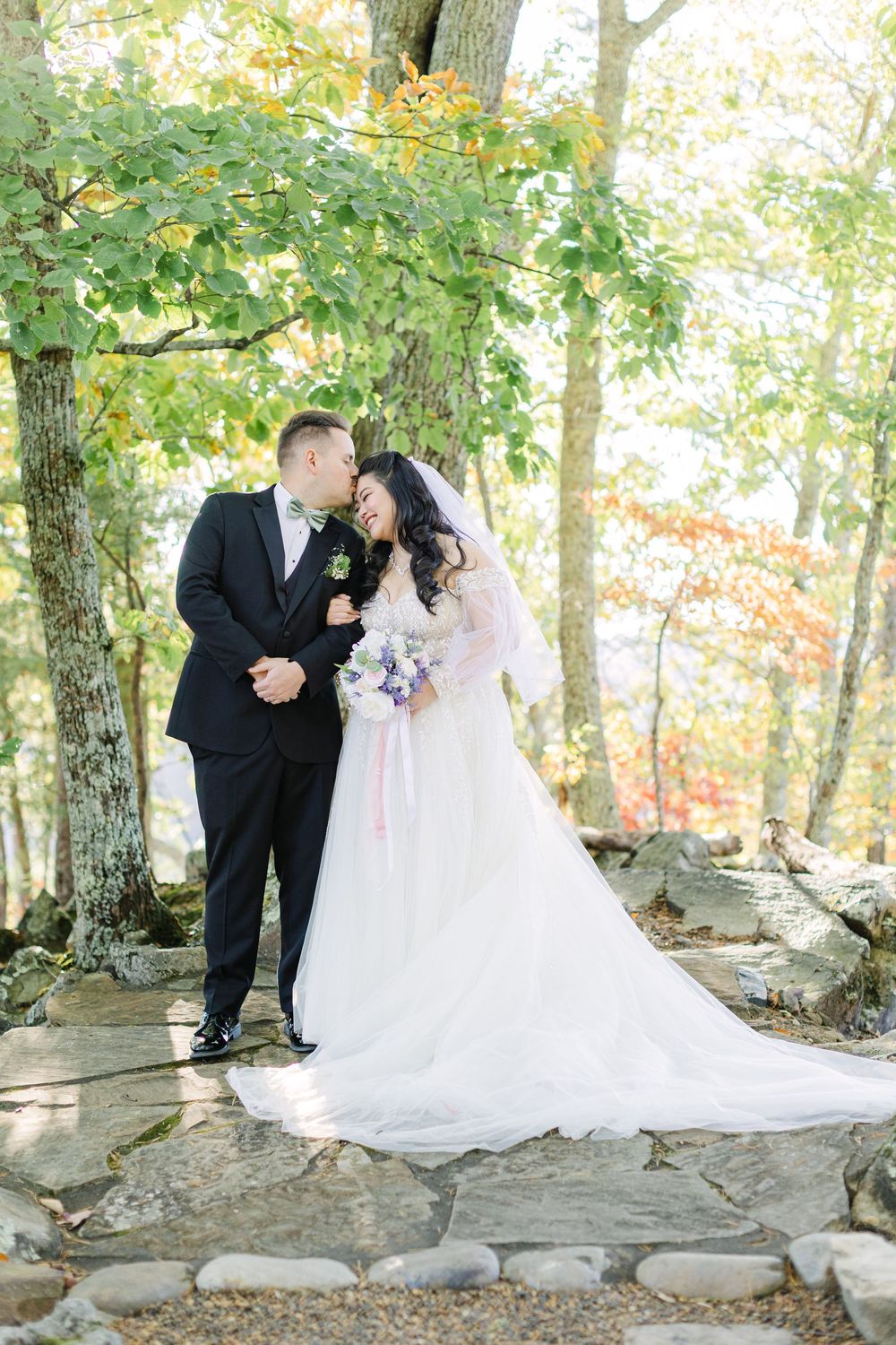 Bride and groom share a romantic moment on a stone patio surrounded by colorful autumn trees.