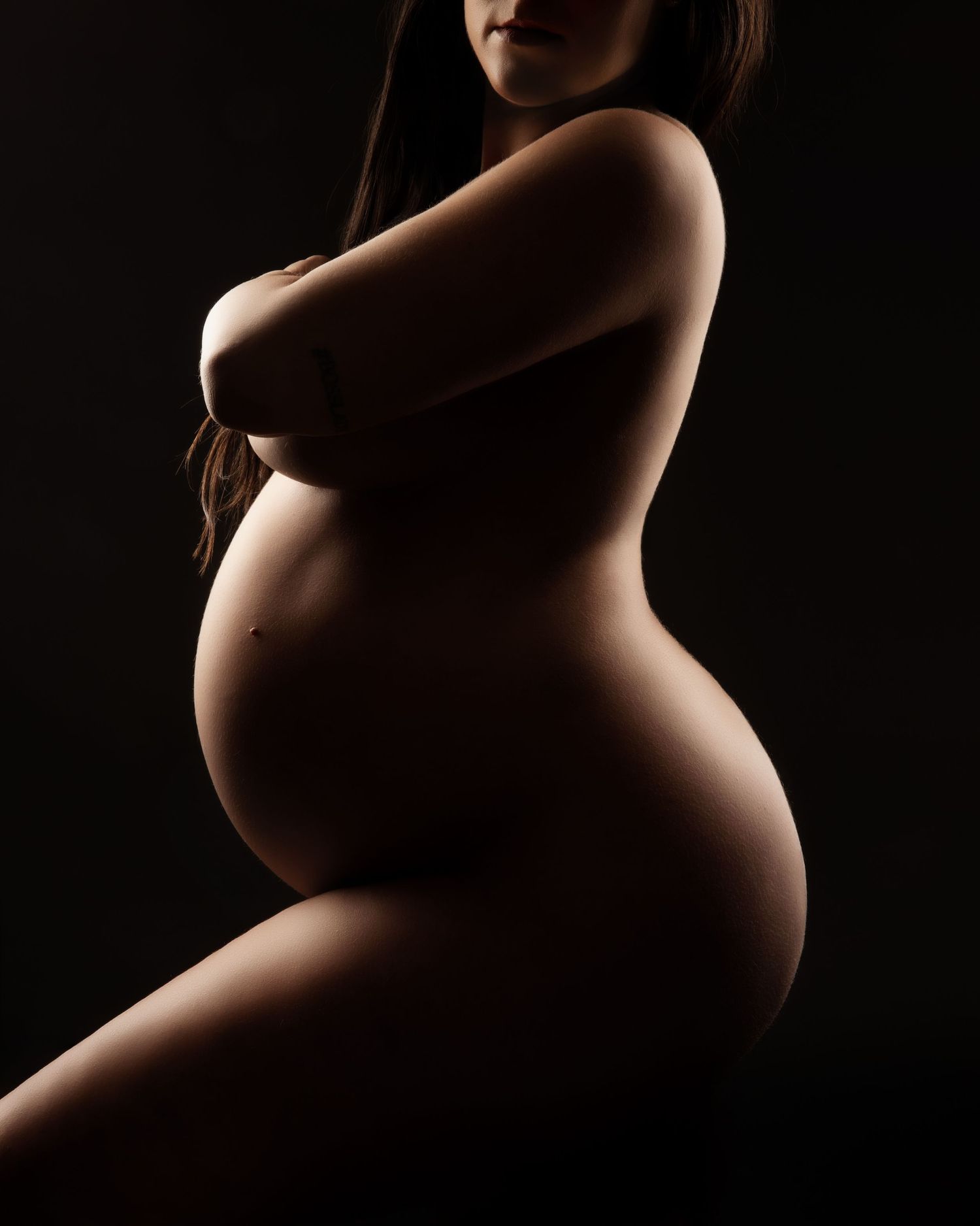Side view maternity silhouette showing the beauty of pregnancy in dramatic lighting.