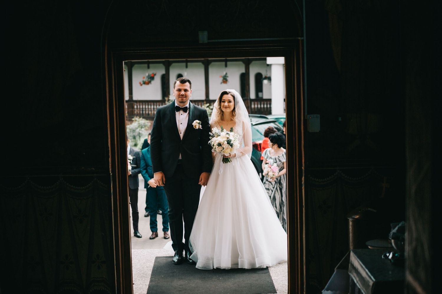 Bride in white ball gown and groom in tuxedo walk through church doorway entrance together.