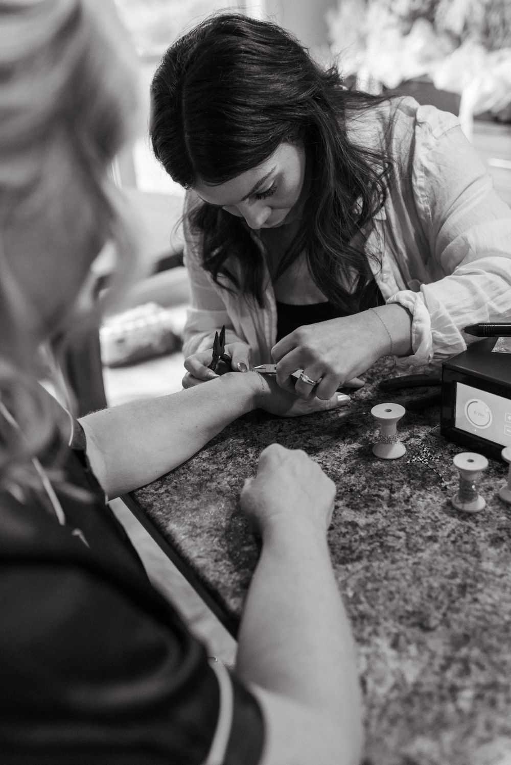 Black and white photo of a woman carefully applying nail art to a client's hand at a salon counter.