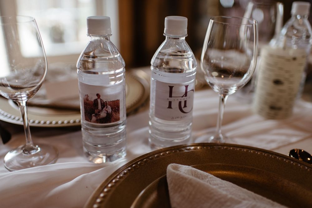 Custom labeled water bottles with monogram and photo labels displayed on elegant wedding reception table setting.