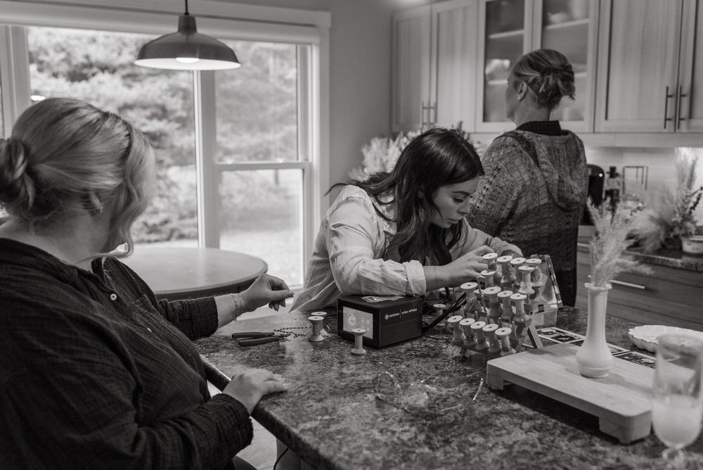 Three women working together in a kitchen, preparing items on a granite countertop in black and white.