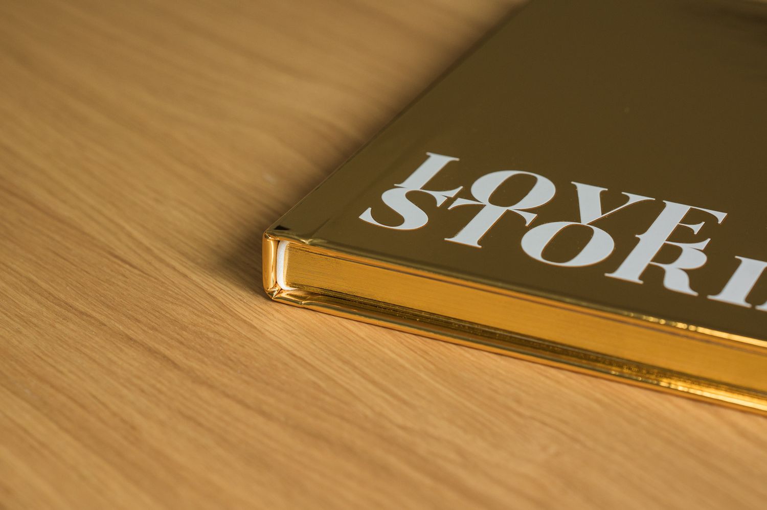 Corner detail of a gold metallic hardcover book titled Love Stories on a wooden surface.