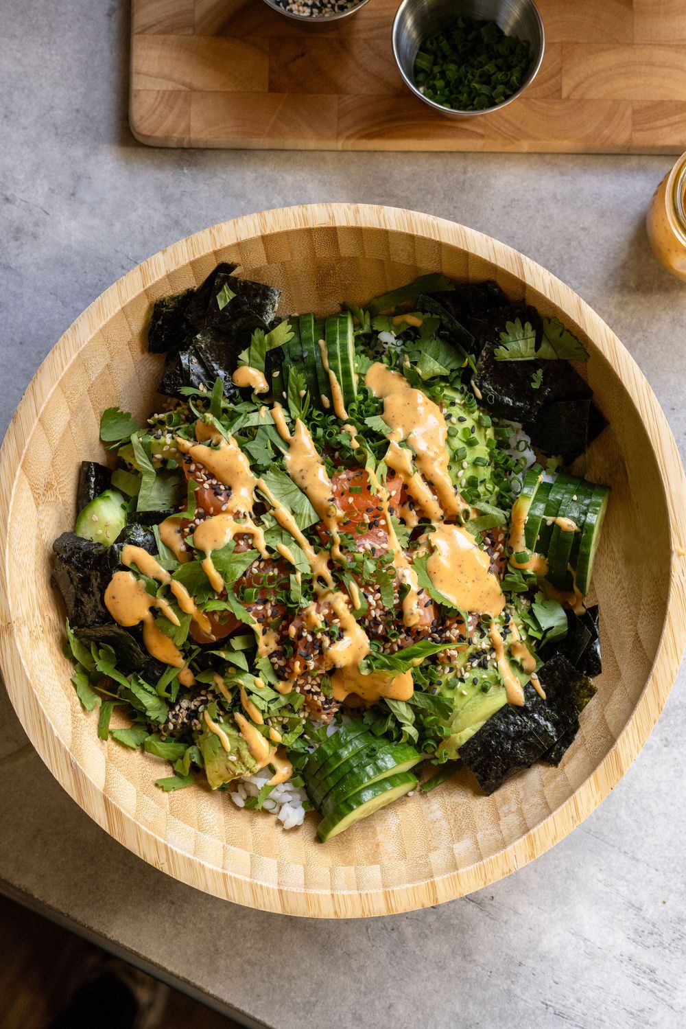 Top-down view of a wooden bowl filled with greens, nori, quinoa, and creamy orange dressing.