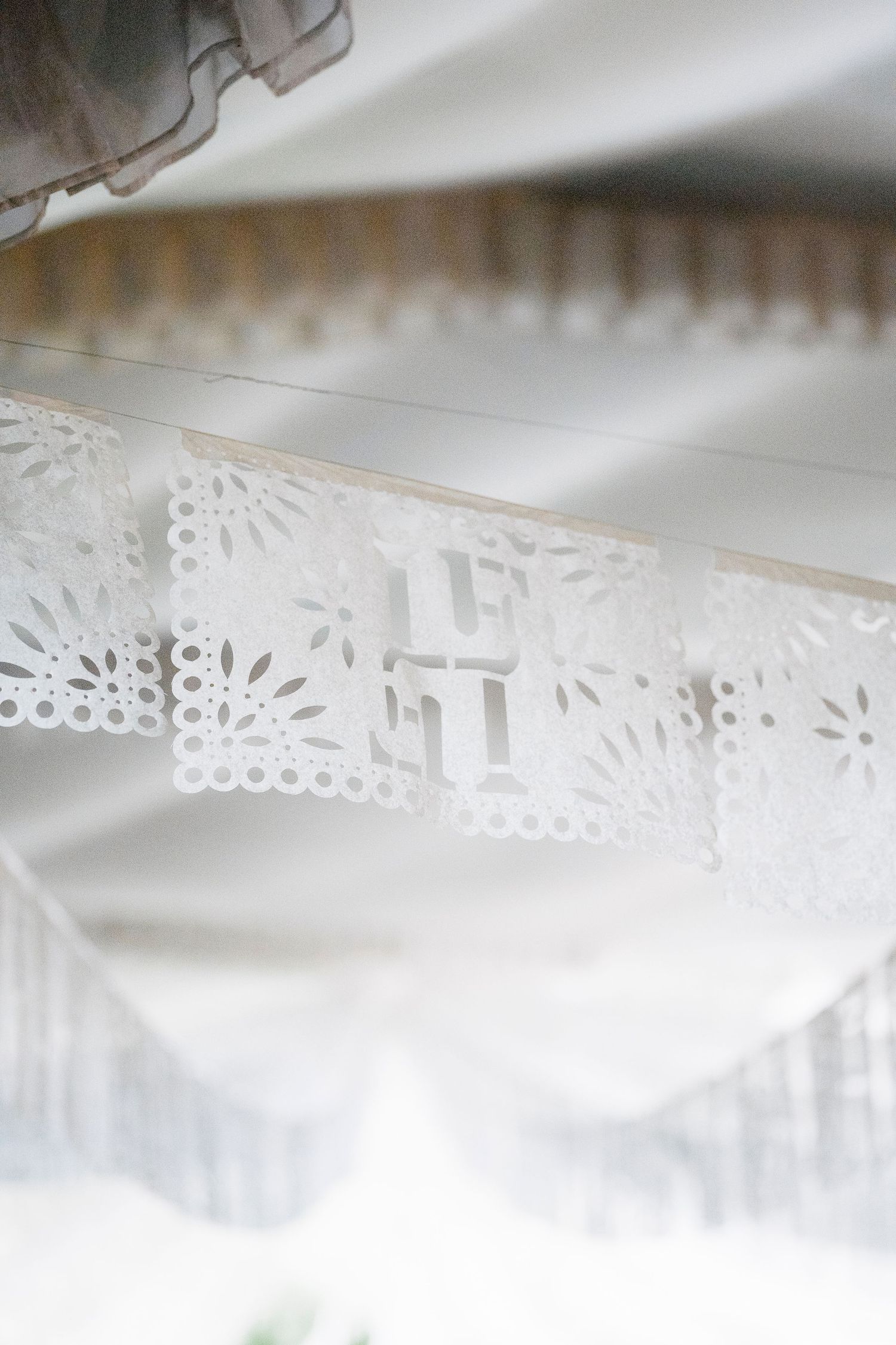 White papel picado banner with intricate cut-out designs hanging under a tent at an elegant wedding celebration.